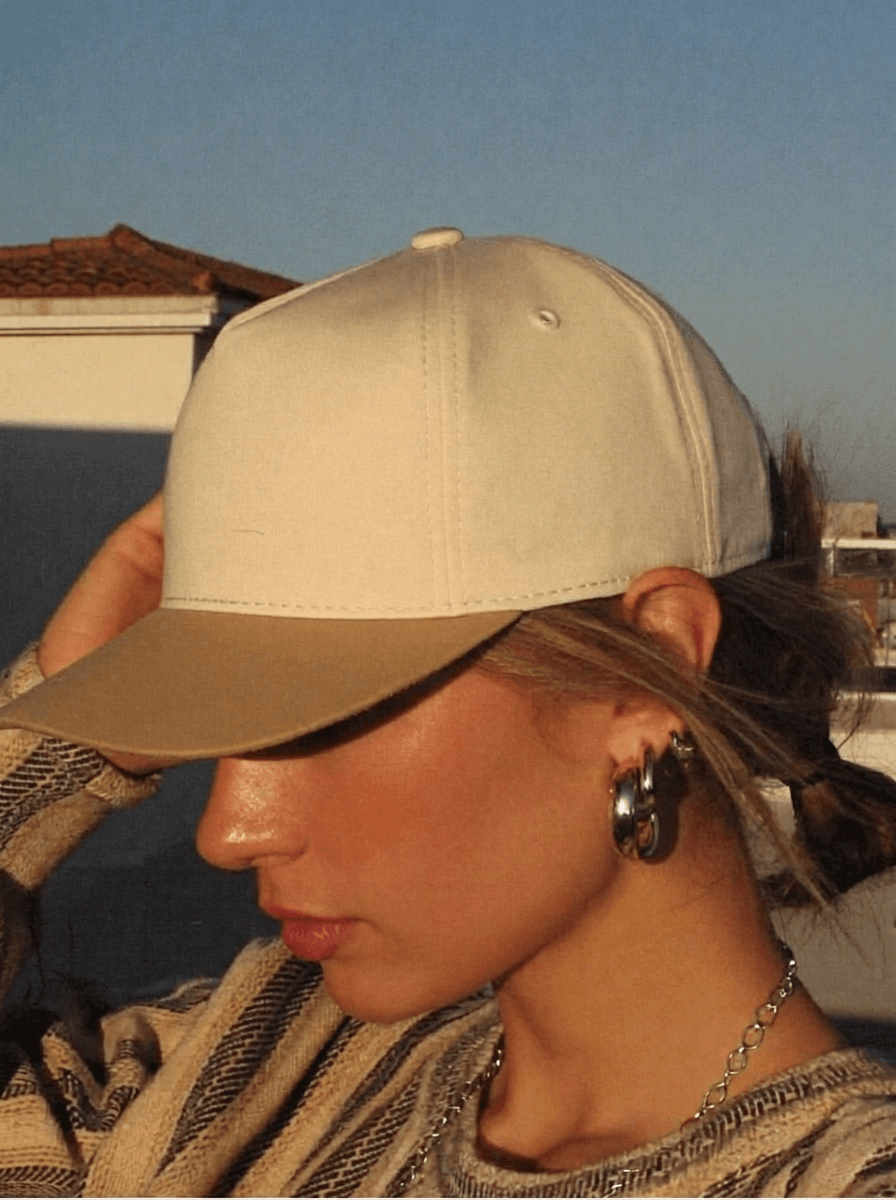 Woman in a cream snapback with gold brim on a rooftop at golden hour