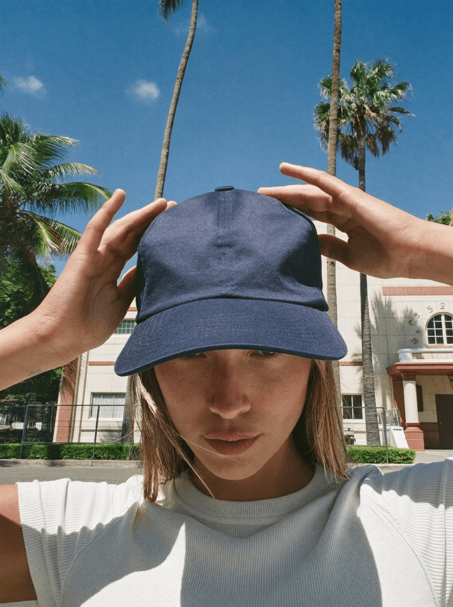 Woman adjusting a navy snapback with Miami architecture behind