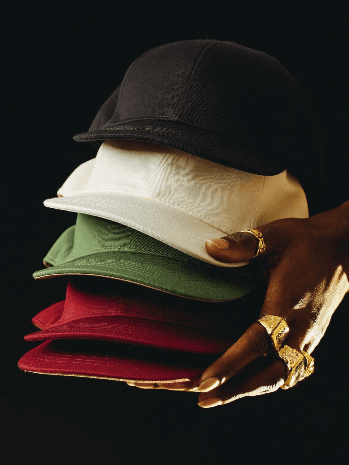 Hands with gold rings holding a stack of snapback caps